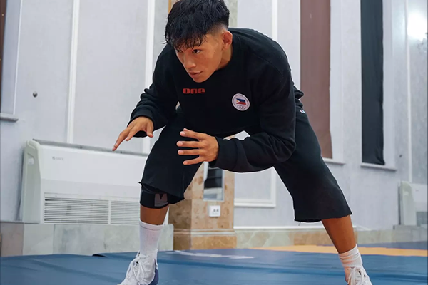 Wrestler Hayden Ancheta in a crouched stance on the mat, eyes locked straight ahead