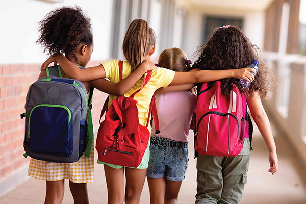 4 children wearing backpacks embracing 