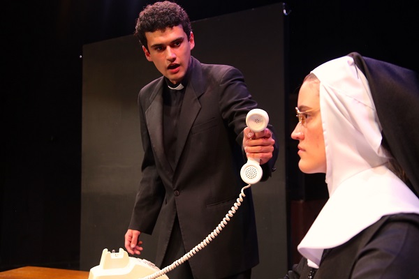 A man dressed like a priest holds a phone out toward a nun