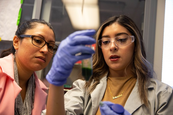 Two female students look at a vial of green liquid