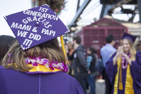 A graduating student has "first generation - gracias - mami and papi we did it" written on her cap