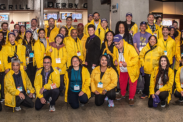 SFSU President Lynn Mahoney stands among a group of commencement ambassadors, all dressed in yellow jackets.