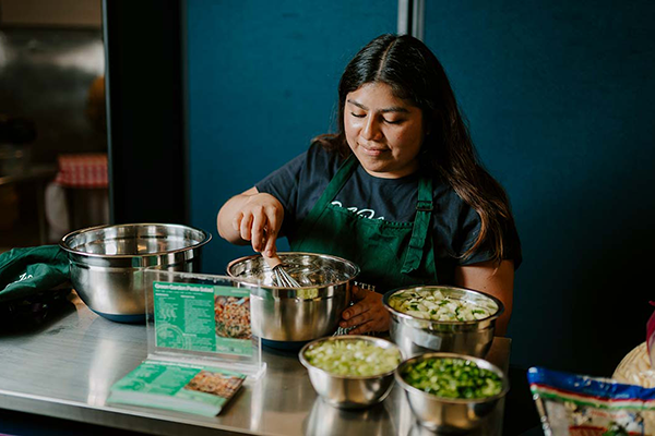 Woman whisking salad dressing while standing and wearing a green apron