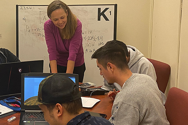 Stephanie Claussen smiles as she engages with engineering students gathered around laptops.