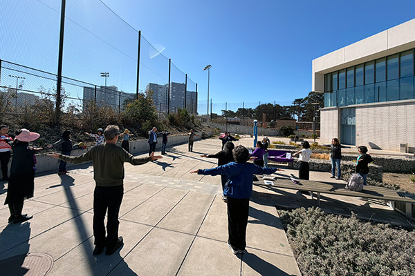 SFSU staff and faculty alumni stretch outside the Mashouf Wellness Center during a wellness event.