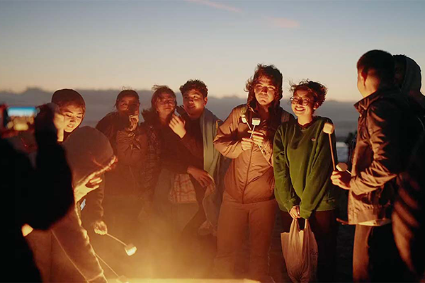 a group of students surrounding a bonfire and making s'mores treats