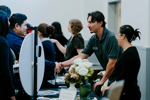 A man shakes hands with an attendee across a table at a SFSU networking event.