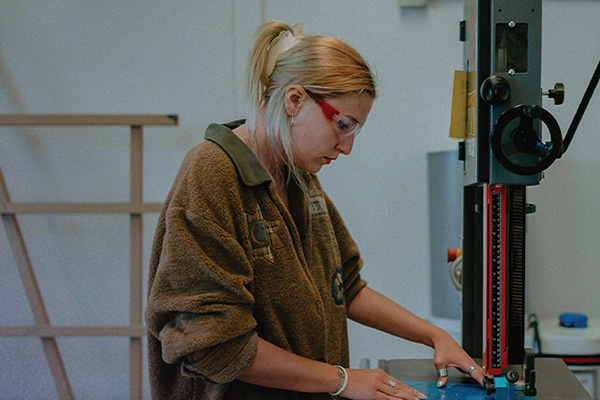 A student wearing safety goggles uses a band saw to make a cut