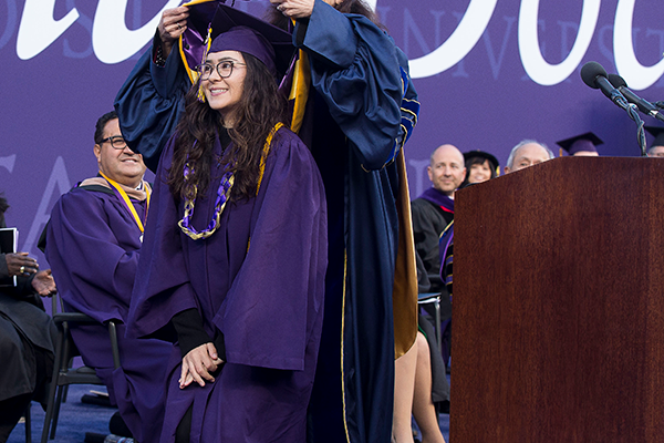 A graduate receives the symbolic investiture of the hood on the Commencement stage