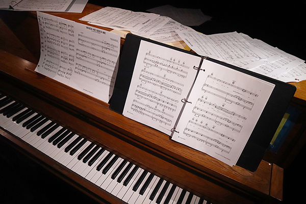 Close-up view of an upright piano, keyboard and sheet music arranged and scattered on top.