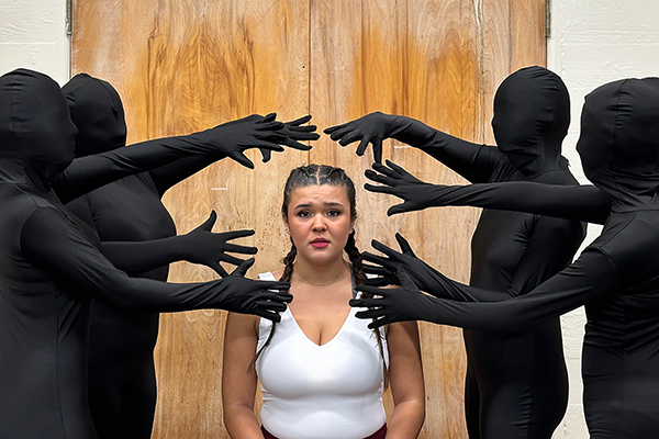 A woman in a white dress surrounded by 4 people wearing black full-body morph suits