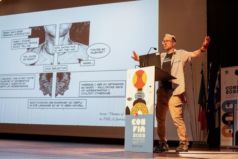 Nick Sousanis stands behind a podium with arms outstretched, presenting illustrations