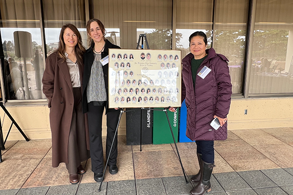 Nursing Alumni pose next to photo featuring past alumni