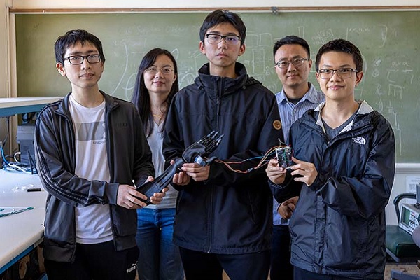 Five people stand with a robotic arm