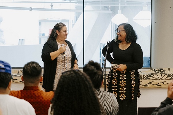 Two smiling women stand at the front of a crowded room 