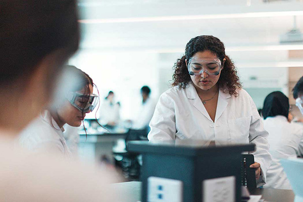 Students wearing white lab coats and safety goggles conducting experiments in a classroom at the Science and Engineering Innovation Center.