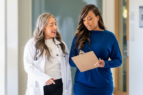 Two healthcare professionals discussing information on a clipboard while walking