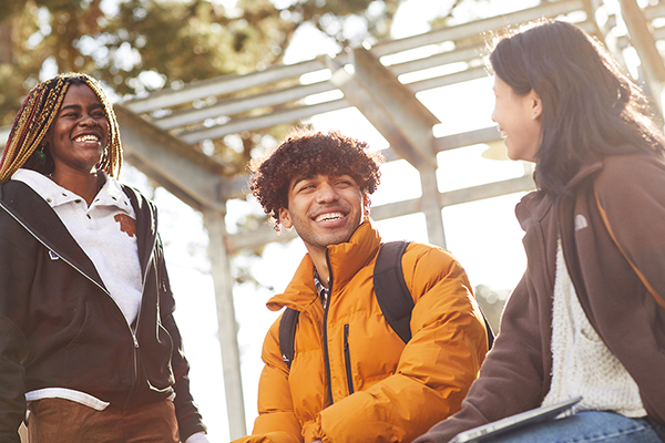 Three SFSU students laughing together outdoors on a sunny day