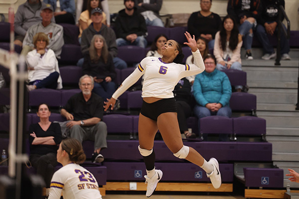 An SFSU volleyball player jumps while in game action with an audience sitting in the bleachers behind her