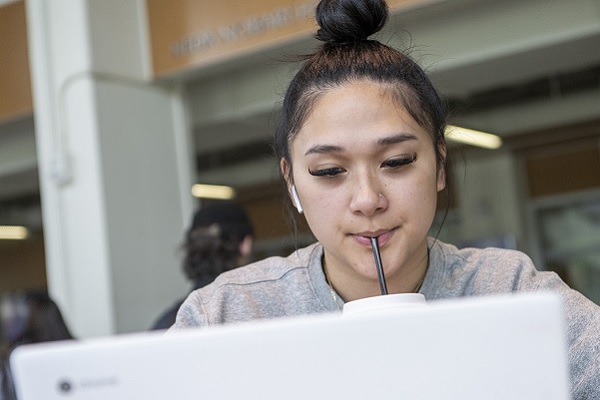 A woman sips on a straw while looking at a laptop