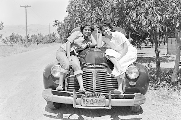 Two women in the countryside smiling sitting and posing on a car