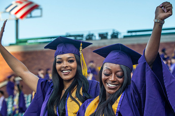 Two students in caps and gowns celebrate during commencement.