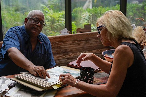 Two people examining printed photographs in a scene from the film Upstream, Downriver.
