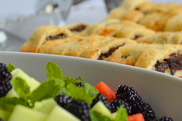 Fresh salad with mint and berries alongside a sliced pastry-like appetizer with a dark fruit filling, prepared by the Vista Room.
