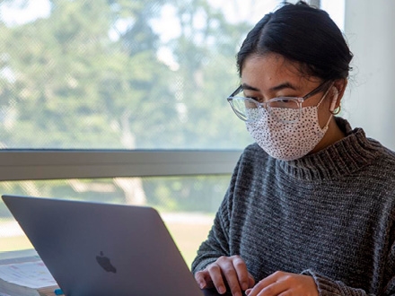 Female wearing a mask and working on her laptop